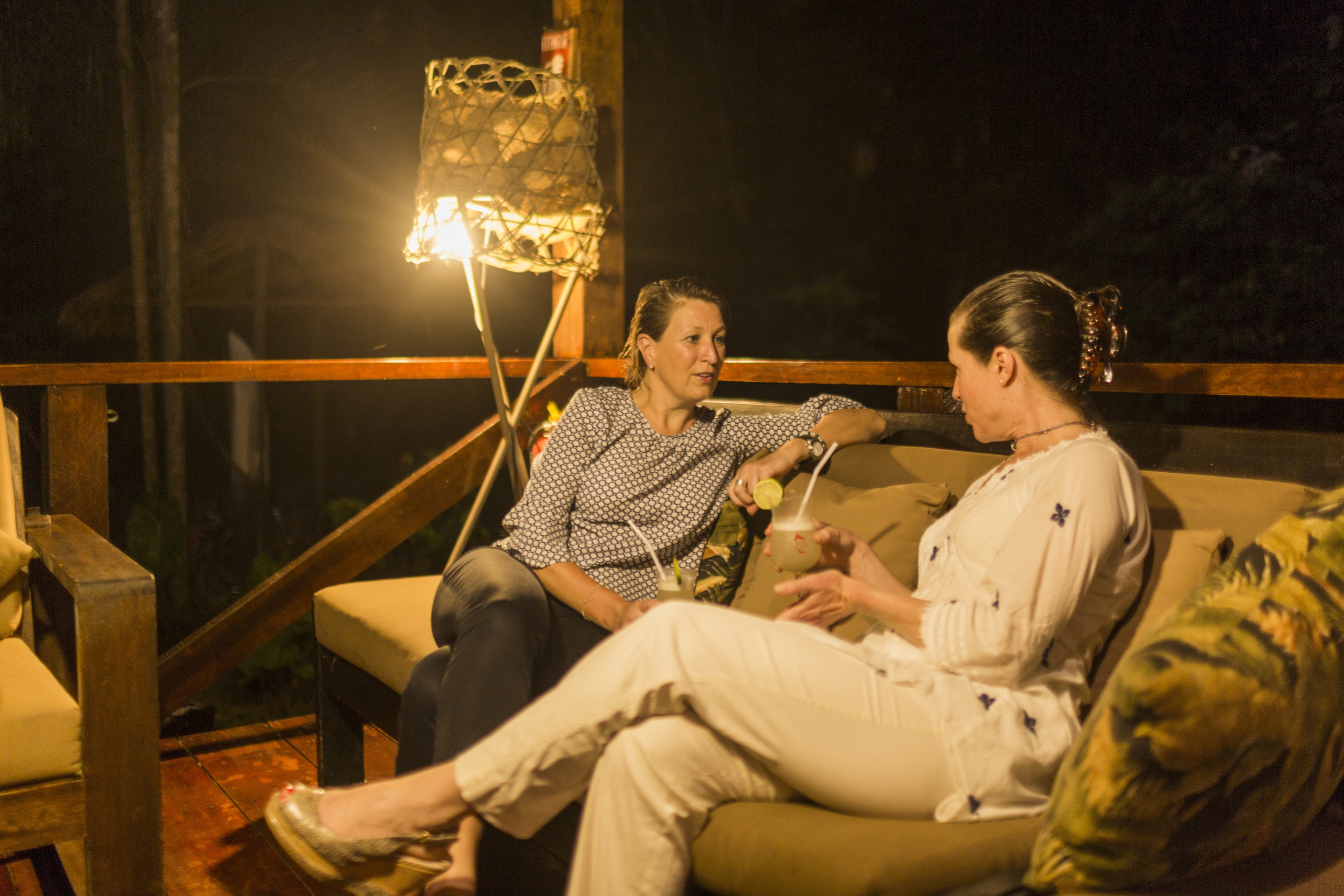 Two women seated and talking at night-time at Refugio Amazonas lodge covered verandah, Tambopata Reserve in Peruvian Amazon rainforest