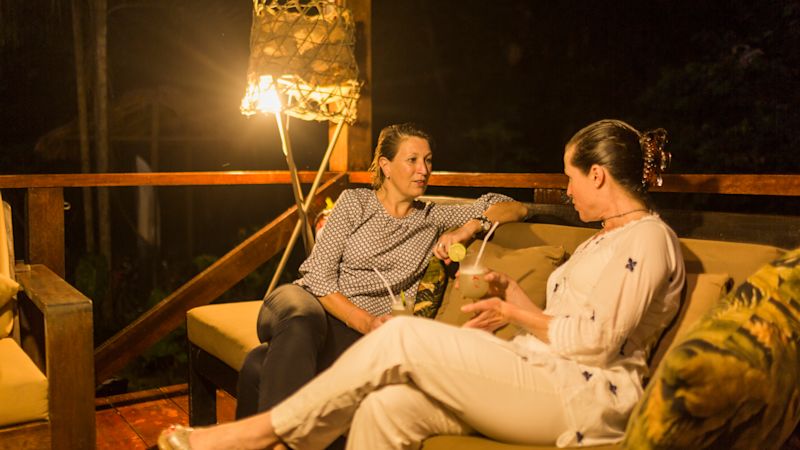 Two women seated and talking at night-time at Refugio Amazonas lodge covered verandah, Tambopata Reserve in Peruvian Amazon rainforest