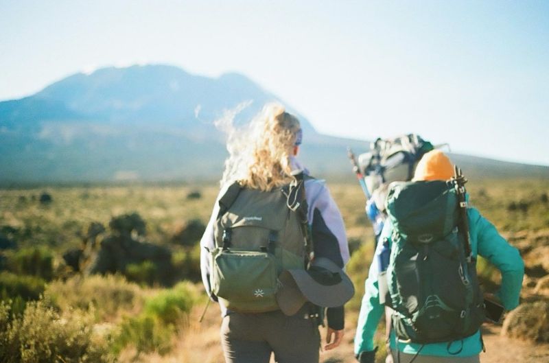 Female hikers wearing backpacks walking towards Kilimanjaro