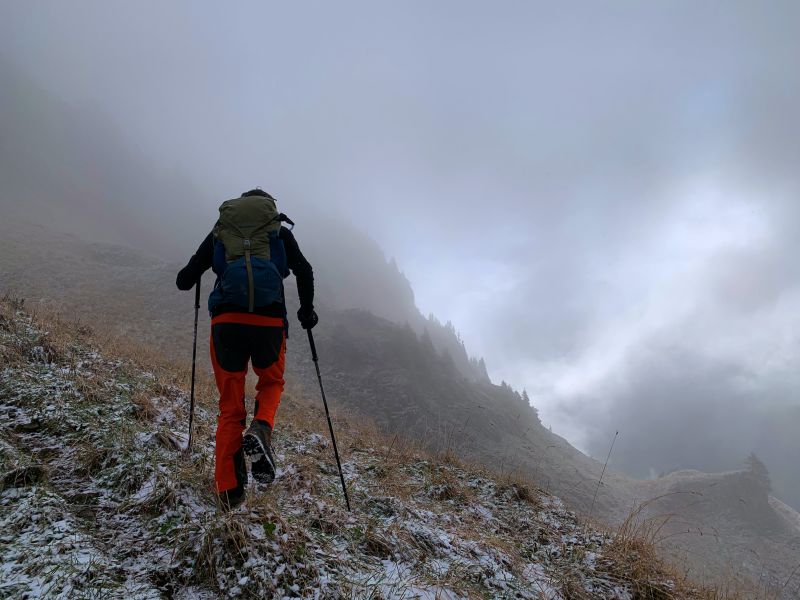 Trekker with trekking poles and backpack in misty mountains