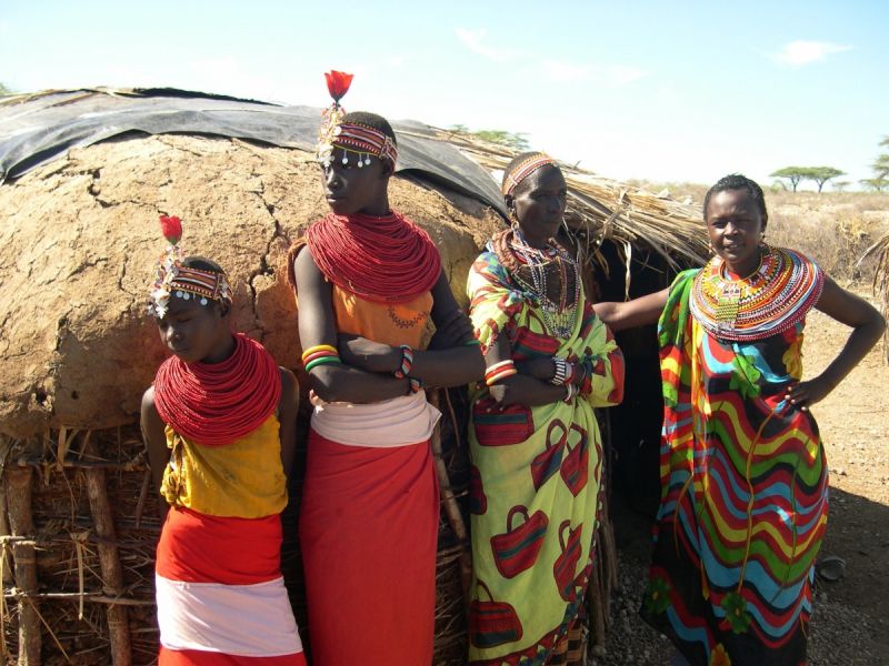 Samburu women and boy standing by traditional mud and thatch hut
