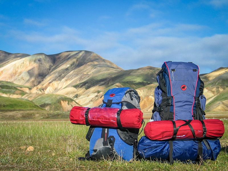 Blue rucksack and blue backpacks on grass with mountains in background