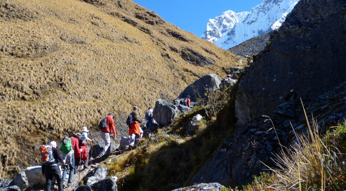 Hikers on a trail along the Salkantay trek in Peru, with a view of snow capped peaks and mountains