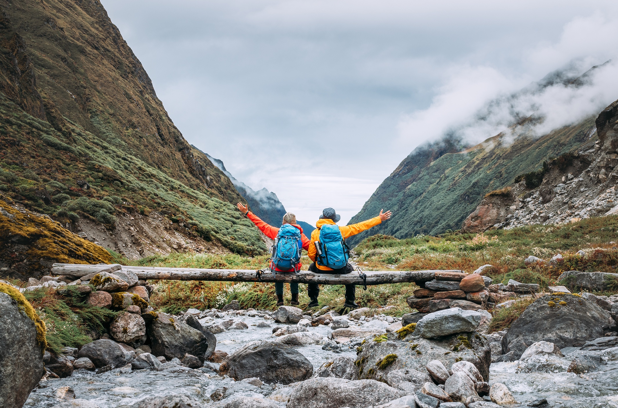 Trekkers Couple sitting on wooden bridge on Mera Peak trekking route near Kothe. Man and woman joyfully raising arms