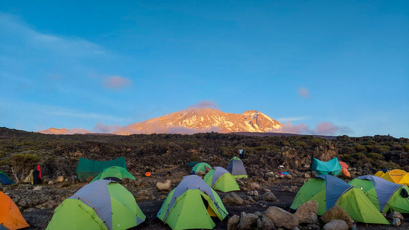 Follow Alice campsite with sleeping tents and toilet tent on Kilimanjaro with Uhuru Peak in background