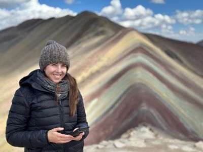 Lady wearing a beanie and smiling at camera on top of Rainbow Mountain, Peru