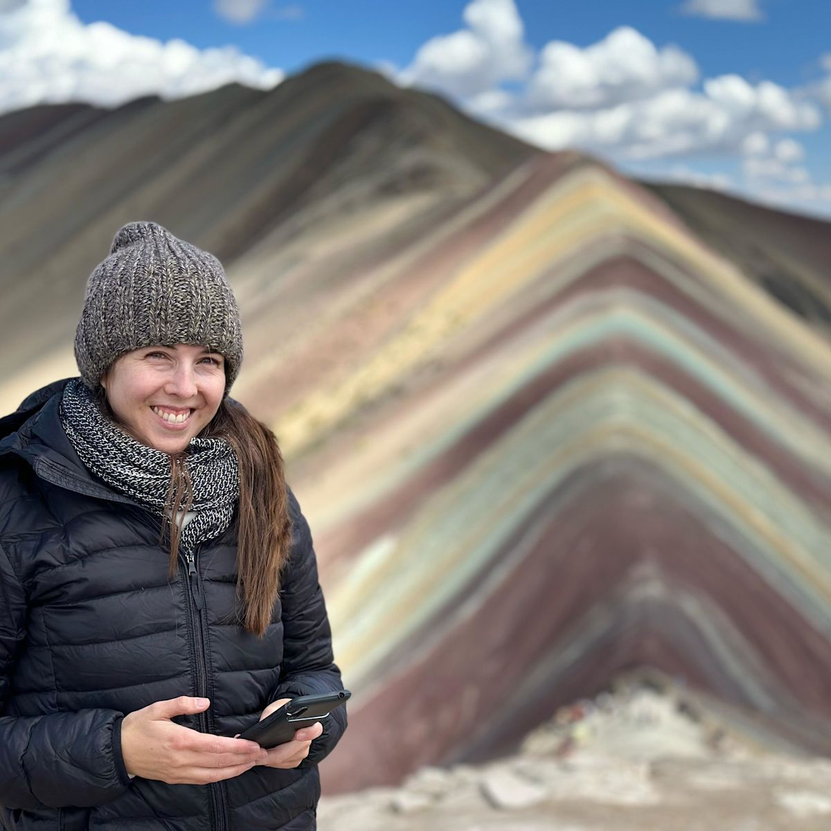 Lady wearing a beanie and smiling at camera on top of Rainbow Mountain, Peru