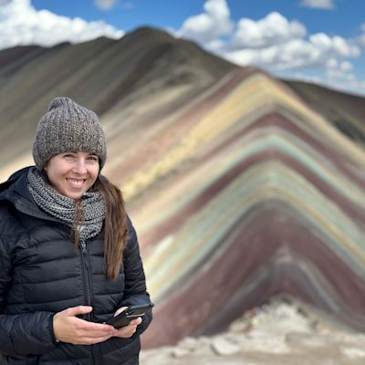 Lady wearing a beanie and smiling at camera on top of Rainbow Mountain, Peru