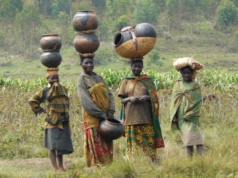 Batwa women and girls standing in a field and balancing pots on their heads