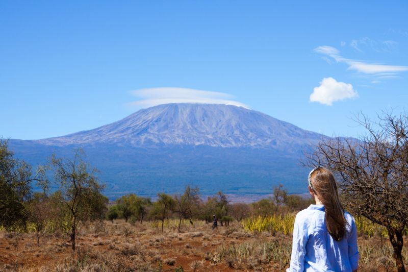 Brown-haired girl wearing blue shirt looking at Mount Kilimanjaro. Clear, sunny day. Amboseli, Kenya