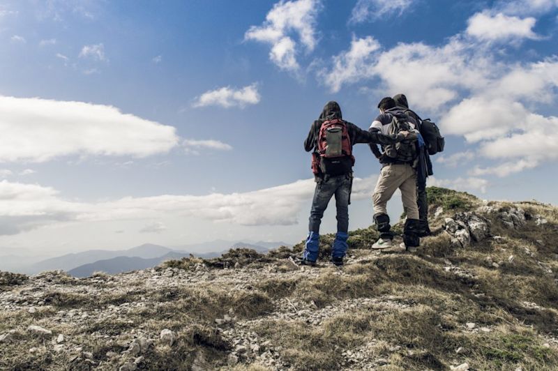 Three hikers stand with their backs to the camera as they look out over the view below