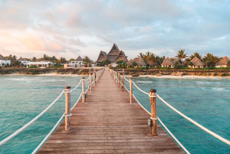 View over ocean coast with wooden bridge, bungalows, palms, pierce at sunrise, Nungwi, Kendwa, Zanzibar island, Tanzania