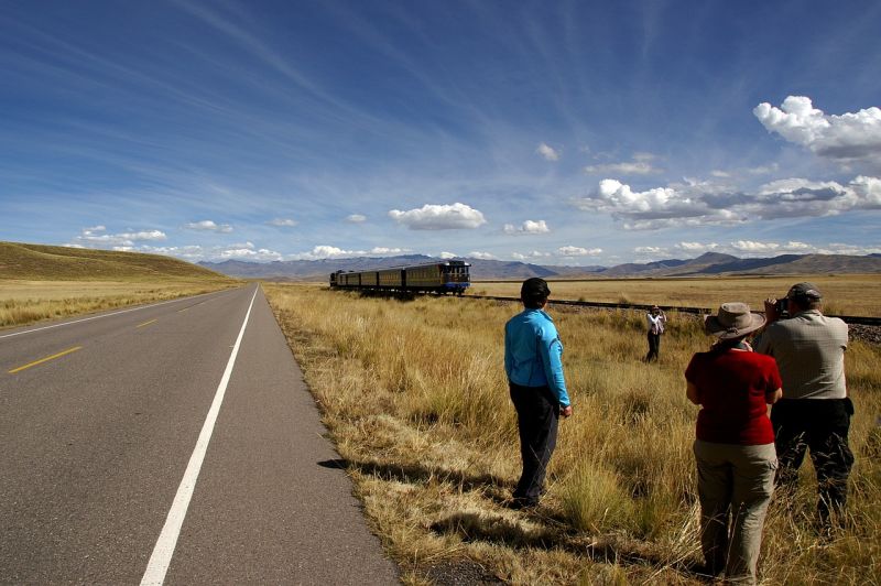 Tourists in Andes of Peru photographing a train on a plateau