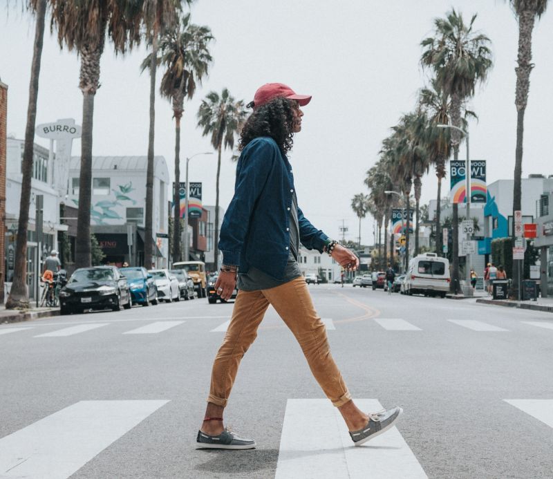 Man in red cap walking across a zebra crossing in a city with palm trees
