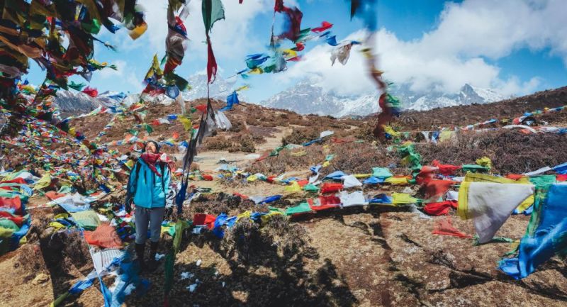 Everest Base camp packing list, woman standing in mountains surrounded by Tibetan prayer flags