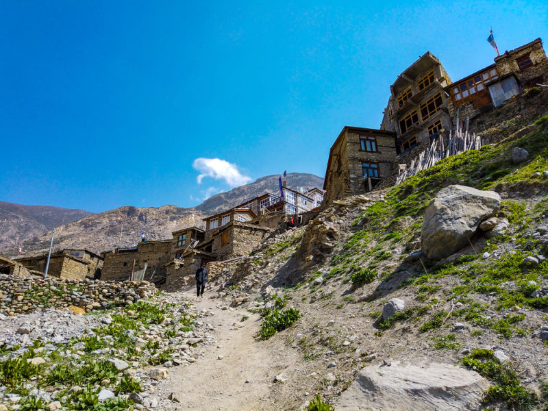 View upwards of trekkers on Annapurna Circuit walking through a village with blue sky, Nepal