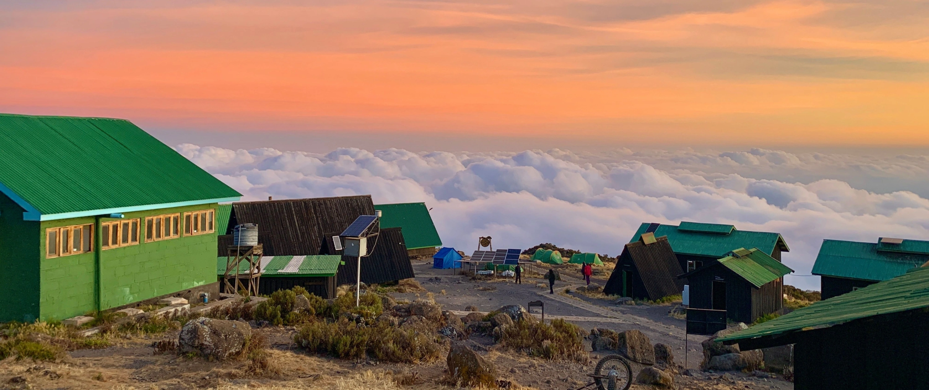 The Horombo Huts on Mount Kilimanjaro with a sea of fluffy clouds around them under a colourful sky