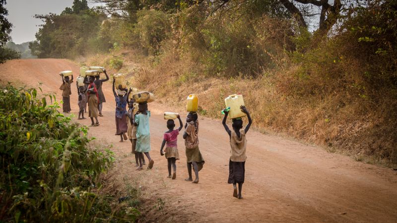 Children carrying water jugs on hand on dusty road in Uganda