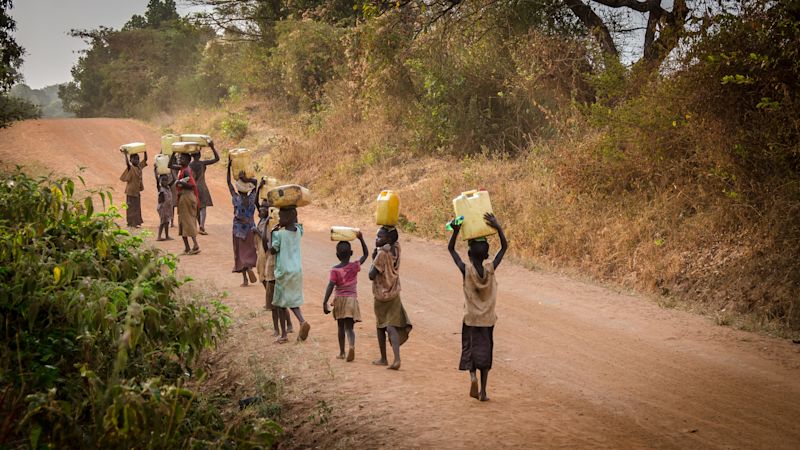 Children carrying water jugs on hand on dusty road in Uganda