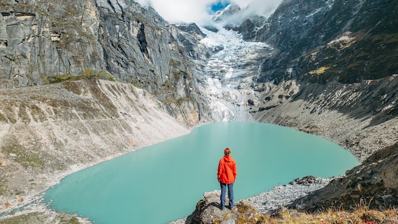 Female trekker dressed bright red jacket on the rock enjoying a glacier falling in high altitude Sabai Tso glacial lake, Makalu Barun National Park, Mera peak climbing route