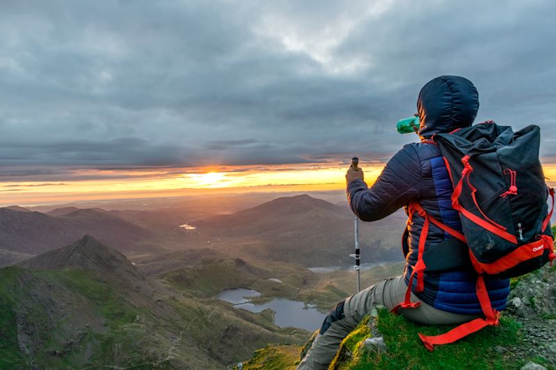 Trekker drinking while seated on a rock looking at the view