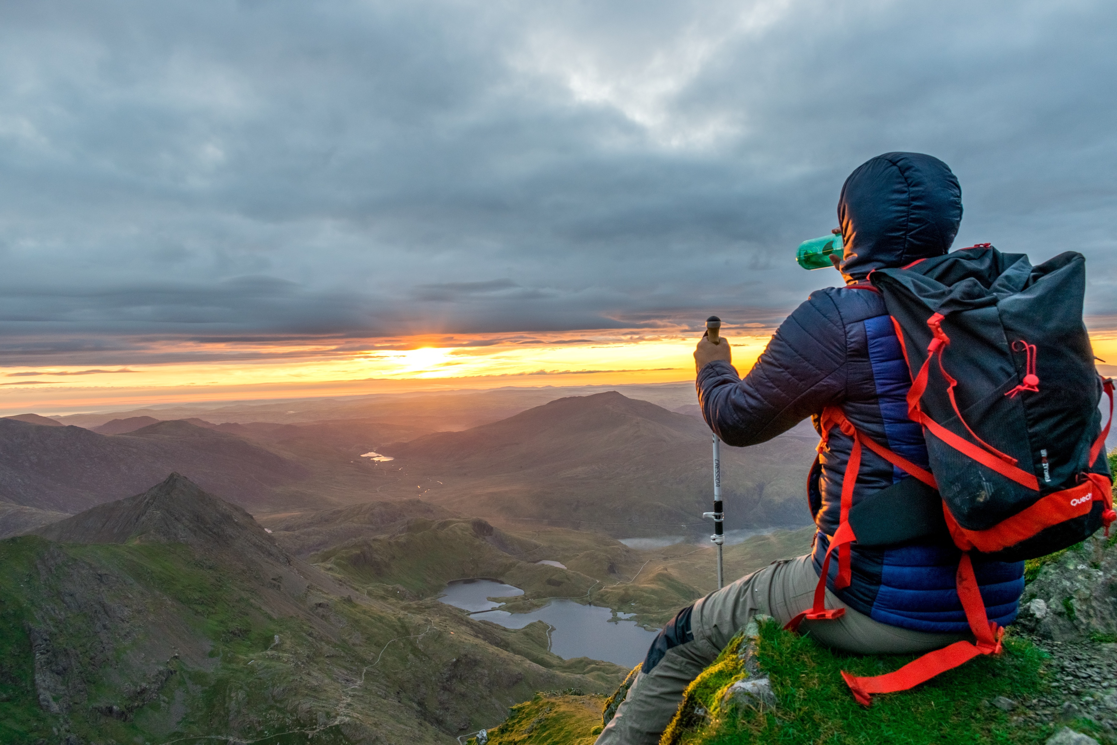 Trekker drinking while seated on a rock looking at the view