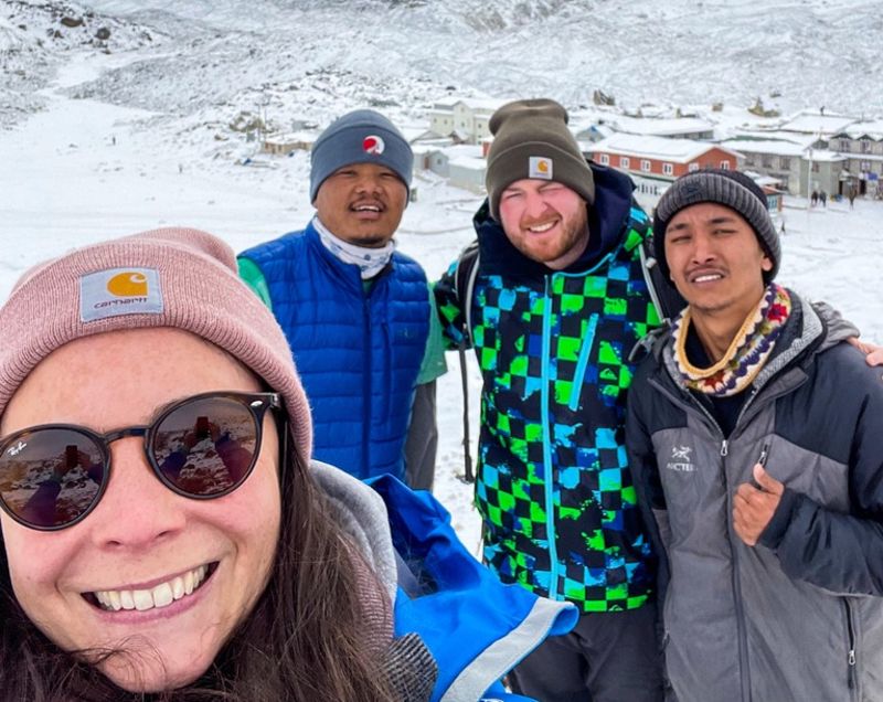 Selfie of smiling group on EBC trek high up in show, Follow Alice trek guide in branded beanie, Nepal 