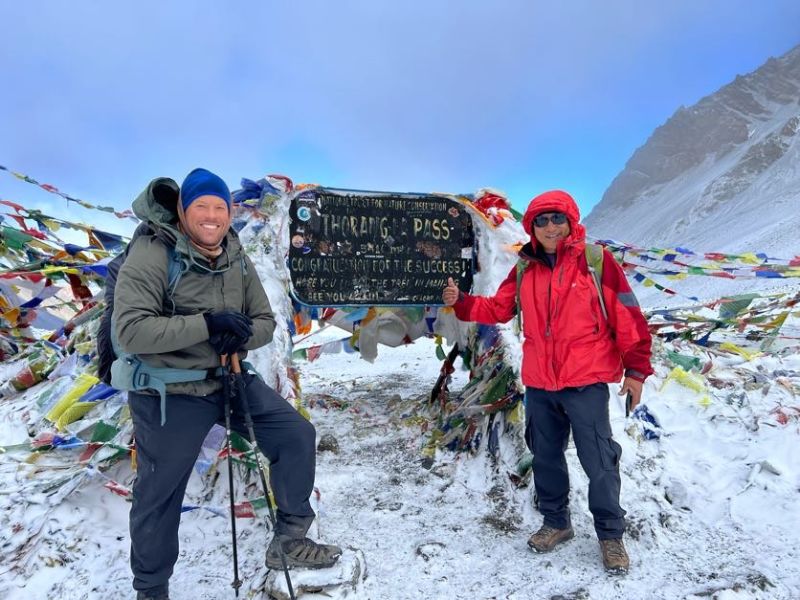 Smiling trekker with guide at Thorung La sign on Annapurna Circuit