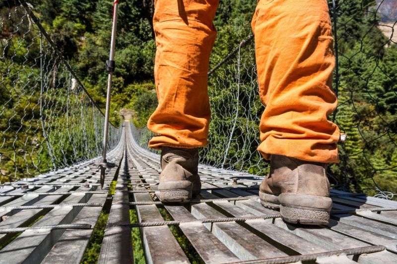 Closeup of boots standing on a suspension bridge. Hiker walking with trekking poles.