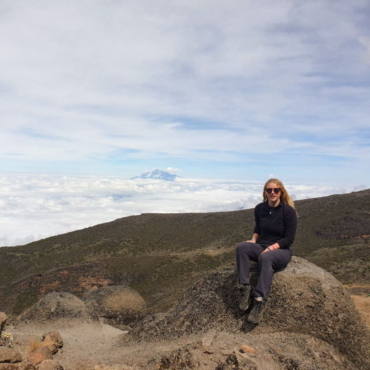 Tash sitting on a rock on Kilimanjaro with cloud bank below