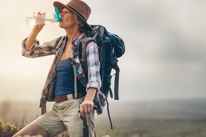 Woman in bush hat drinking water on trek