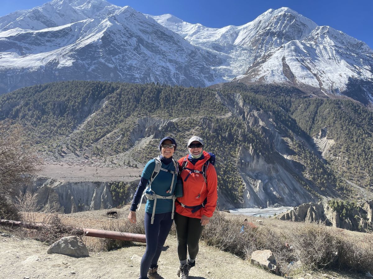 Two trekkers smiling at camera with forests and mountains of Annapurna Circuit behind