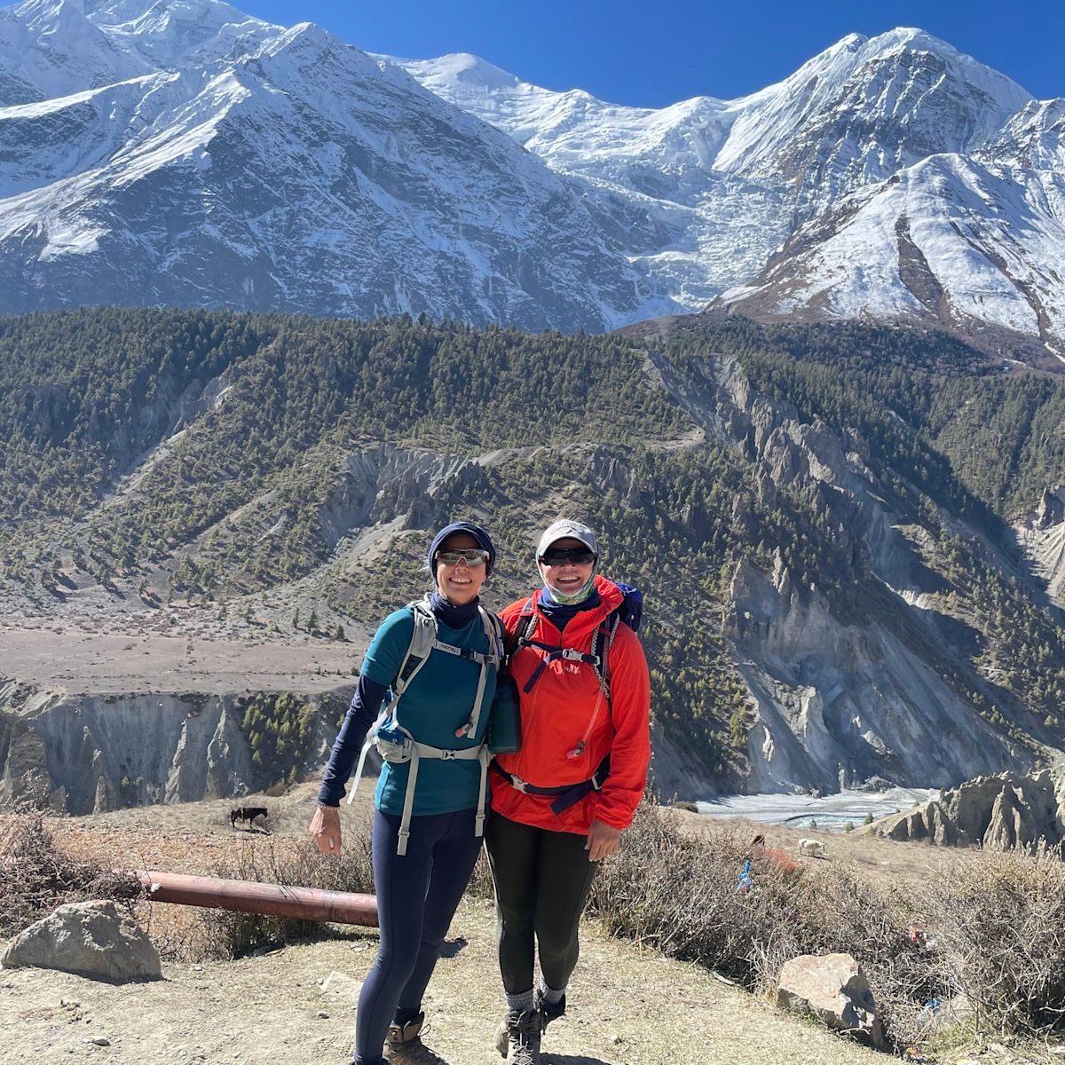 Two trekkers smiling at camera with forests and mountains of Annapurna Circuit behind