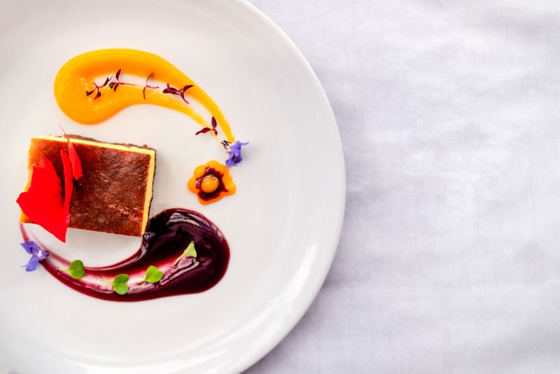 Top view of sweet corn cheesecake with purple corn and mango sauces on a white plate on a white table cloth, Peruvian food