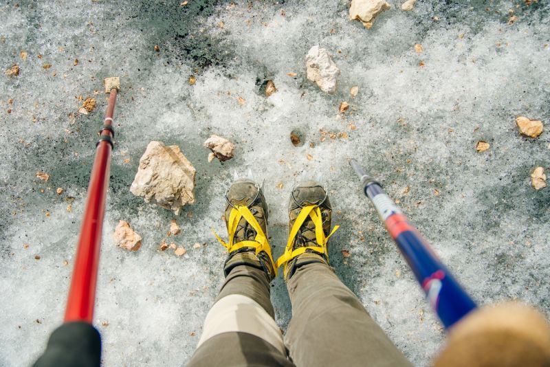 Top view of hiking boots in crampons standing on ice, and trekking poles