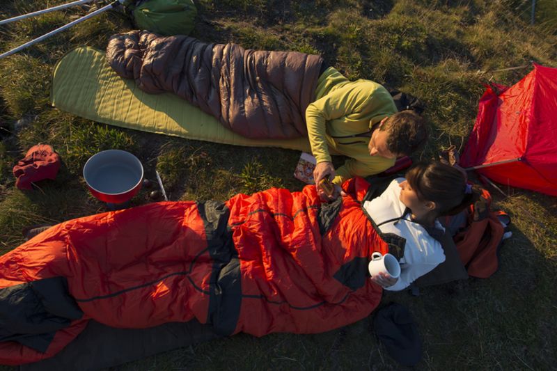 Man and woman in sleeping bags on sleeping mats by tent 