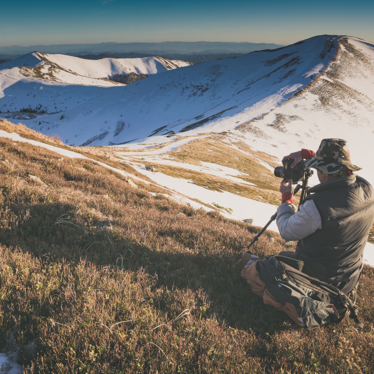 Male trekker taking photo using tripod in snowy high alpine landscape
