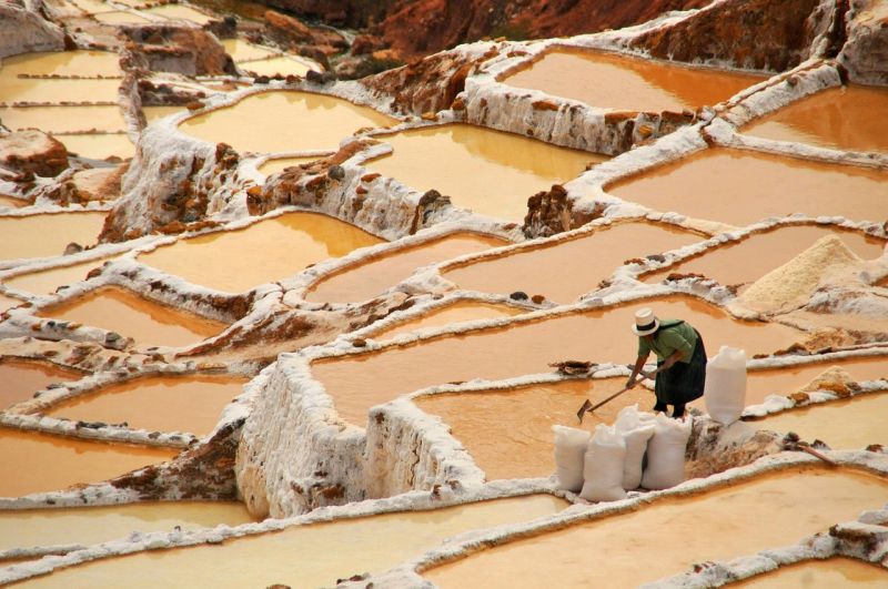 Woman in hat working in the salt mines of Maras in Sacred Valley, Peru