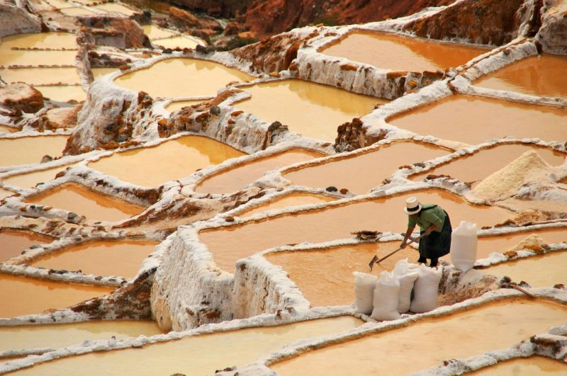 Woman in hat working in the salt mines of Maras in Sacred Valley, Peru