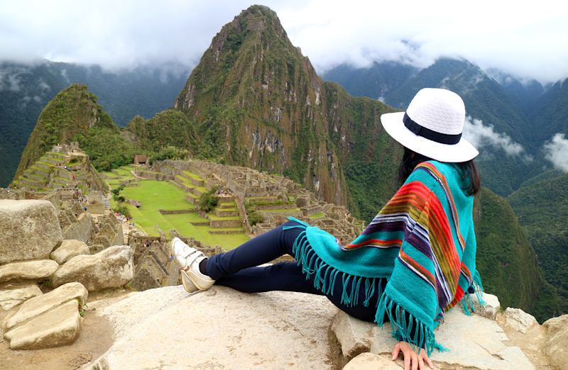 Machu Picchu with Waynapicchu mountain behind it and a seated woman in the foreground