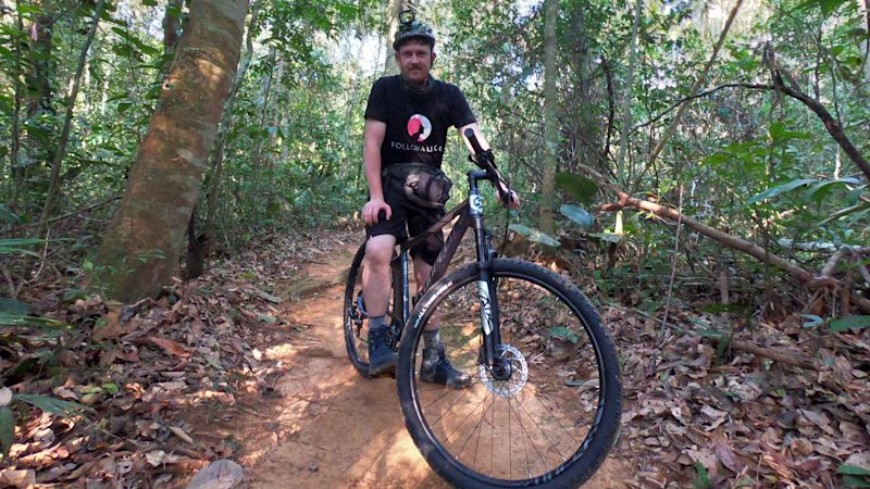 Man in branded Follow Alice T-shirt on a mountain bike on path in Amazon rainforest, Peru