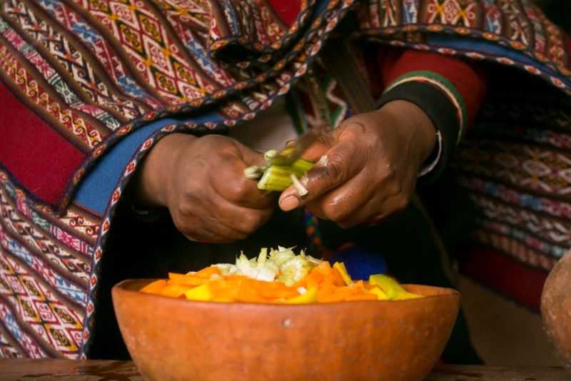 Woman's hands chopping vegetables into a bowl as she prepares a traditional Andean meal, Sacred Valley, Peru