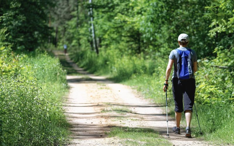 Man backpacker on dirt road walking with trekking poles