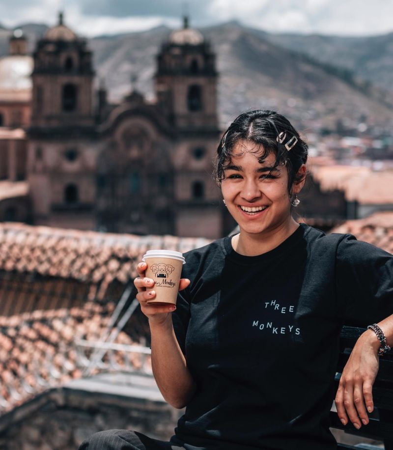 Three Monkeys coffee Cusco, employee with takeaway coffee cup and city behind her