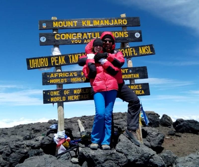 Couple smiling and hugging in front of Uhuru Peak sign on Kilimanjaro
