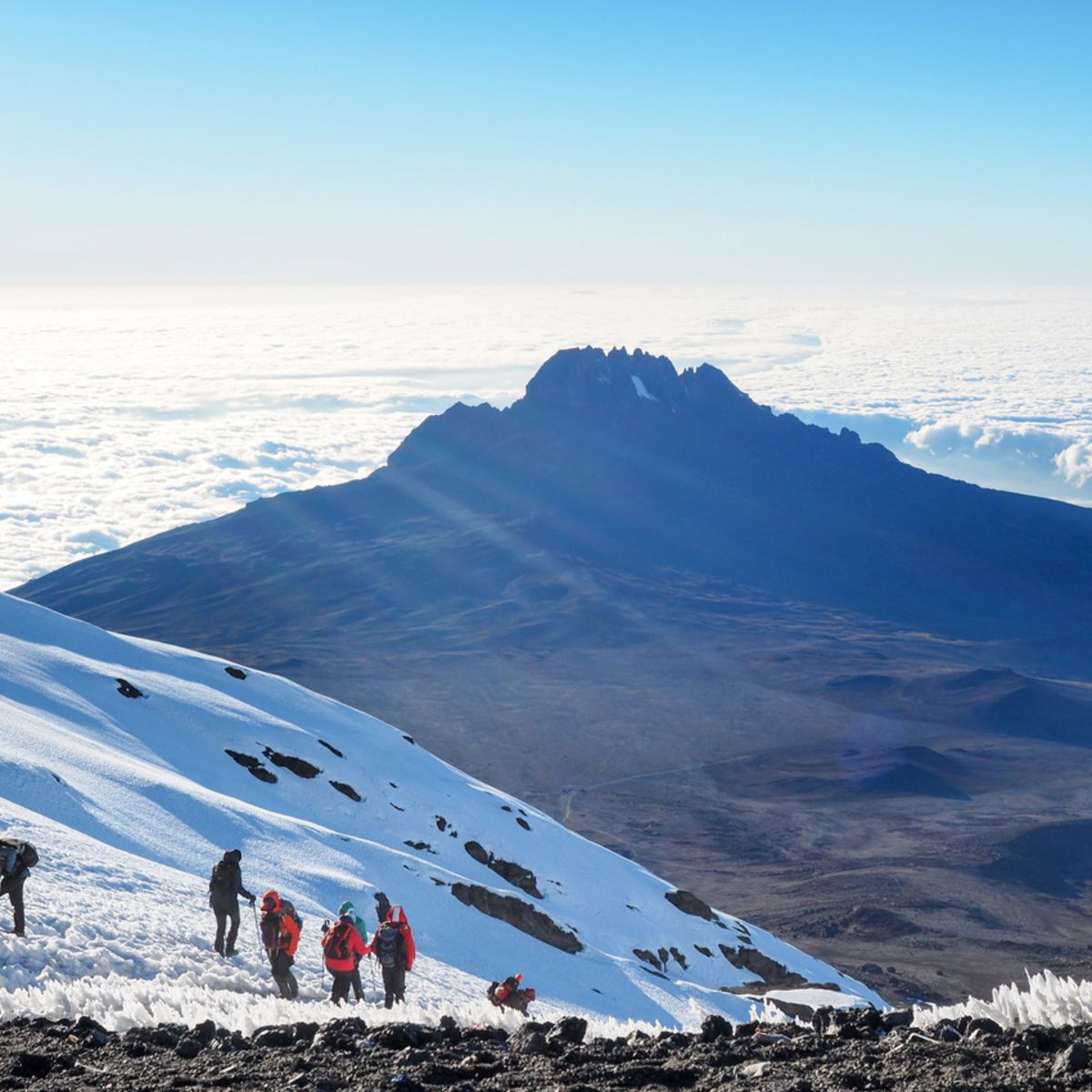 Hikers on the ridge in snow ascend mount Kilimanjaro summit with clouds and Mawenzi in background (1)