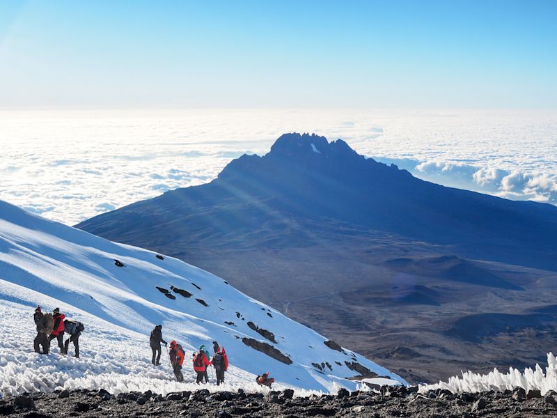 Hikers on the ridge in snow ascend mount Kilimanjaro summit with clouds and Mawenzi in background (1)