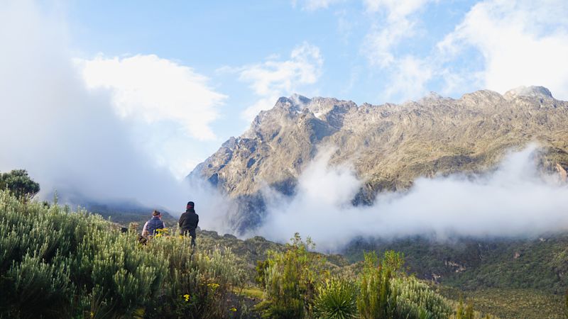 Two trekkers watching sunrise in Rwenzori Mountains in Uganda