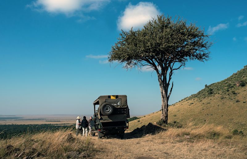 Safari vehicle by lone tree and people standing next to it