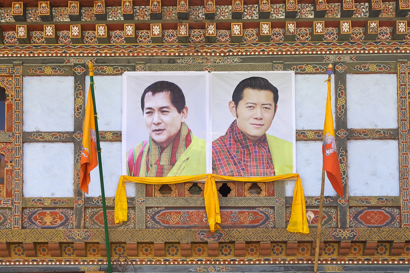 An image of the 4th and 5th Kings of Bhutan, Jigme Singye Wangchuck and Jigme Khesar Namgyel Wangchuck, displayed on the facade of a traditional building in Chhume village, Bhutan.